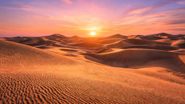 Desert sand dunes at sunset with warm orange sky and soft clouds